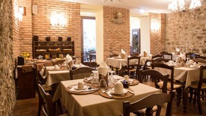 A restaurant with brick walls, wooden tables, and chandeliers. - La Plumeria Hotel (Cefalù)
