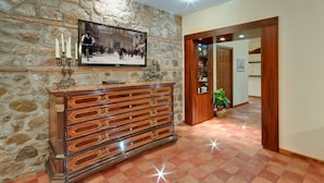 A stone wall with a wooden dresser, a television, and a potted plant in a hallway. - La Plumeria Hotel (Cefalù)