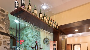 A bar area with a wooden counter, wine bottles, glasses, and a decorative wall. - La Plumeria Hotel (Cefalù)