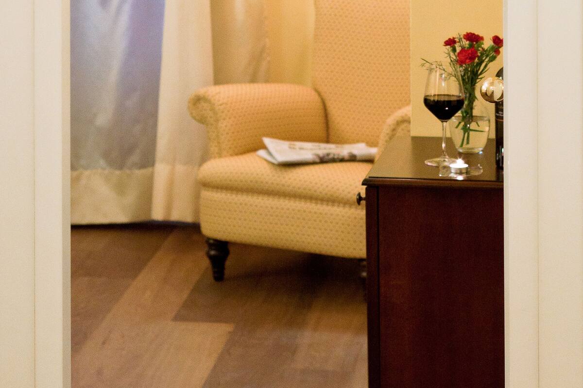 Een kamer met een beige fauteuil, een houten kast en een lijst met een afbeelding aan de muur.