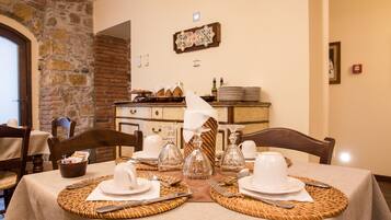 A dining table set with white plates, silverware, and glassware, with a stone wall and a wooden cabinet in the background.