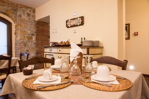 A dining table set with white plates, silverware, and glassware, with a stone wall and a wooden cabinet in the background.