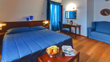 Quarto de hotel com uma cama grande, uma mesa de trabalho, uma cadeira e uma pequena mesa com uma tigela de fruta.