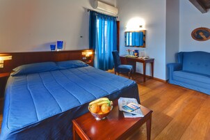 Quarto de hotel com uma cama grande, uma mesa de trabalho, uma cadeira e uma pequena mesa com uma tigela de fruta.