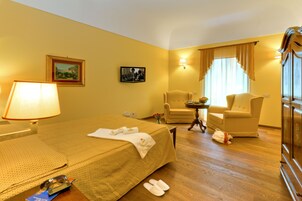 Una habitación de hotel con una cama, dos sillones, una mesita y una lámpara.