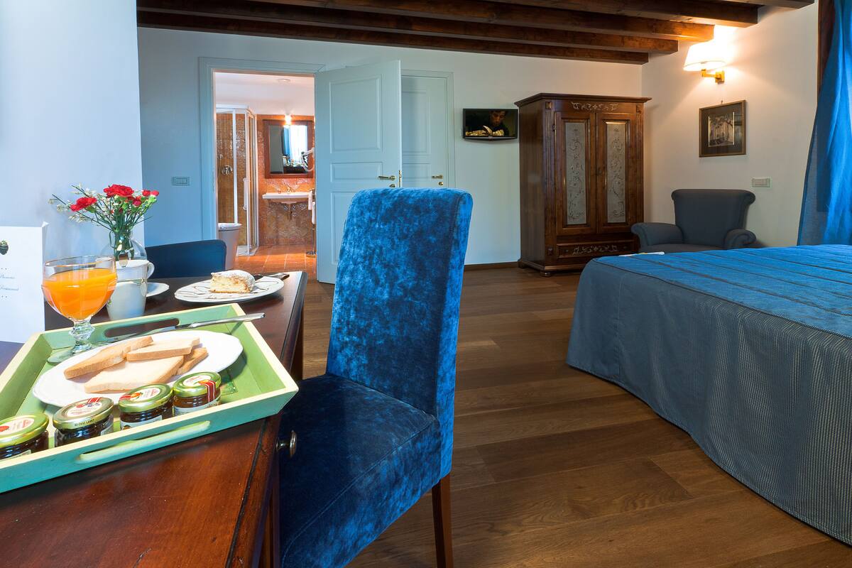 Een hotelkamer met een bed, een eettafel met ontbijtartikelen, een blauwe stoel en een houten kast.