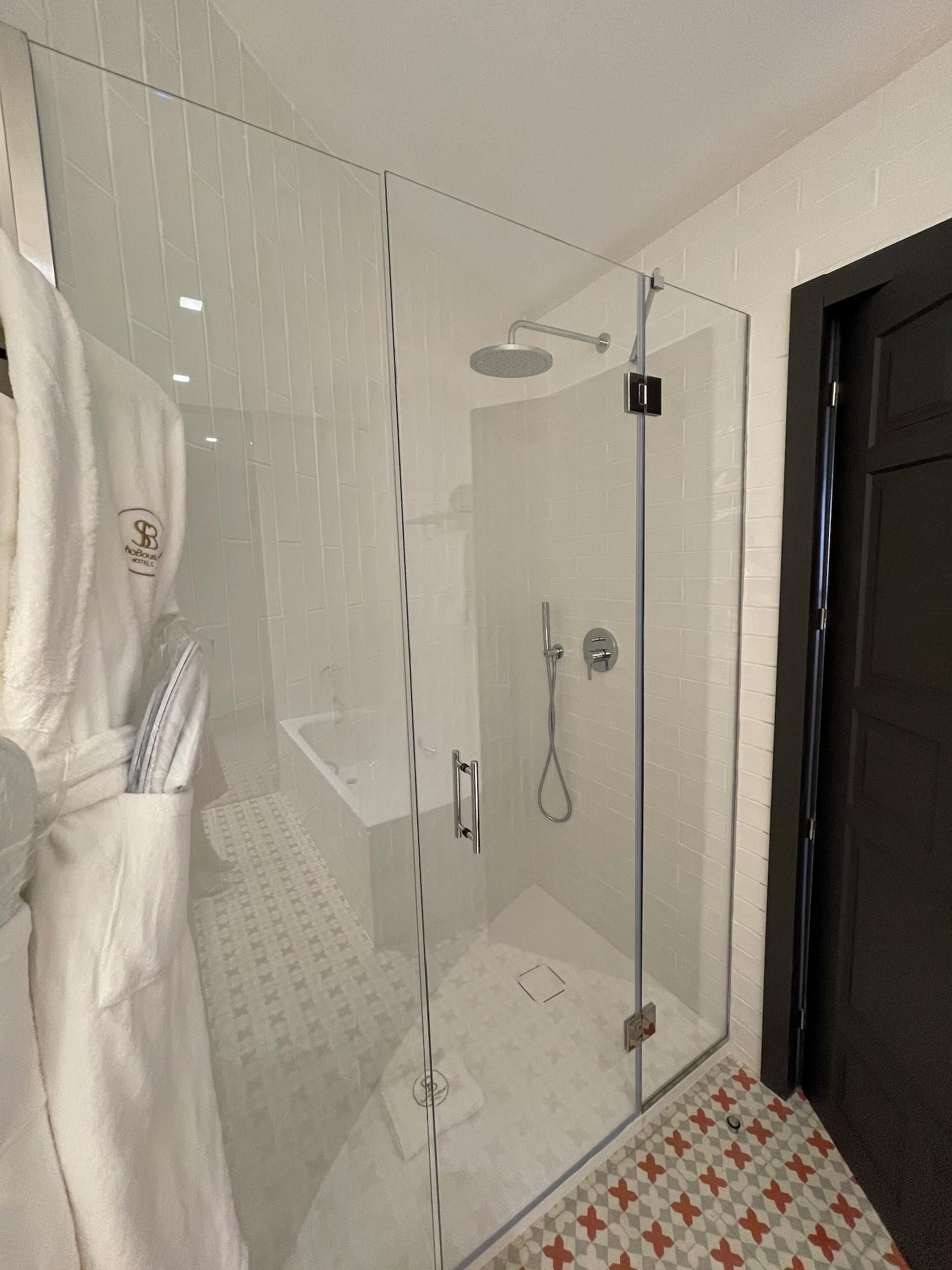A glass-enclosed shower with a handheld showerhead, a glass door, and a towel rack with a robe hanging on it.