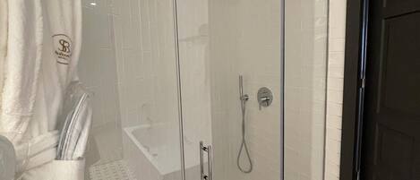 A glass-enclosed shower with a handheld showerhead, a glass door, and a towel rack with a robe hanging on it.