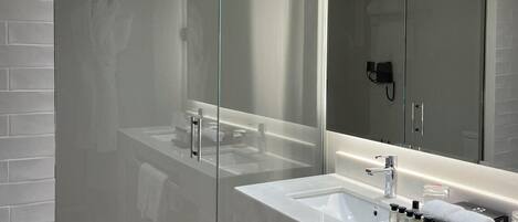 A modern bathroom with a glass shower enclosure, a large mirror, and a vanity with a sink and towel rack.