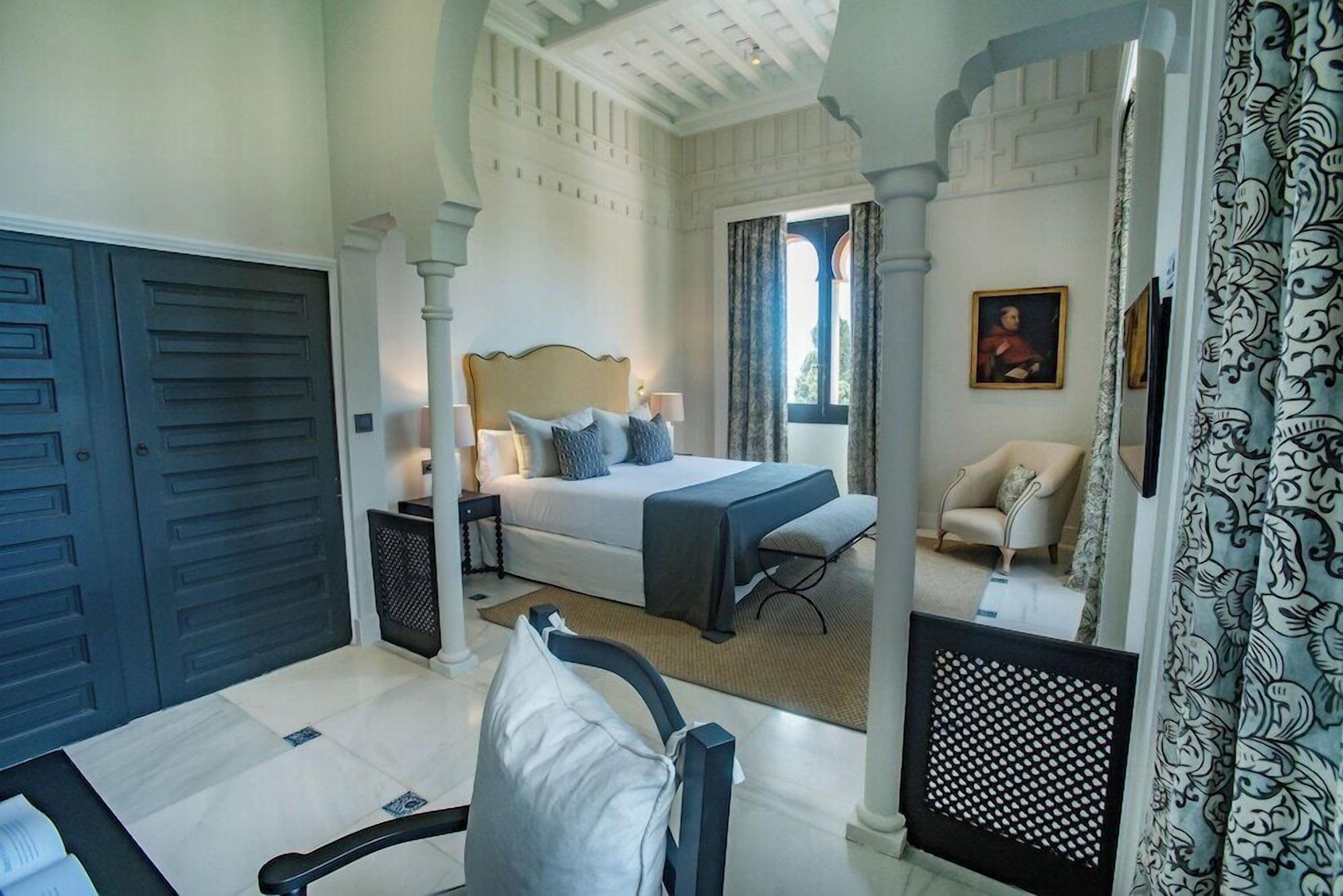 A bedroom with a bed, nightstands, a chair, and a view through an archway.
