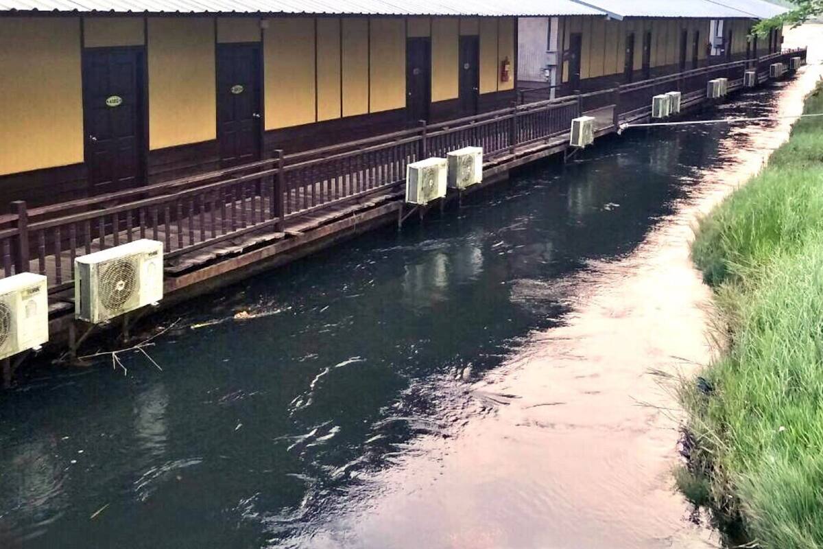Een lang gebouw met een houten terras en airconditioners langs een smal waterkanaal.