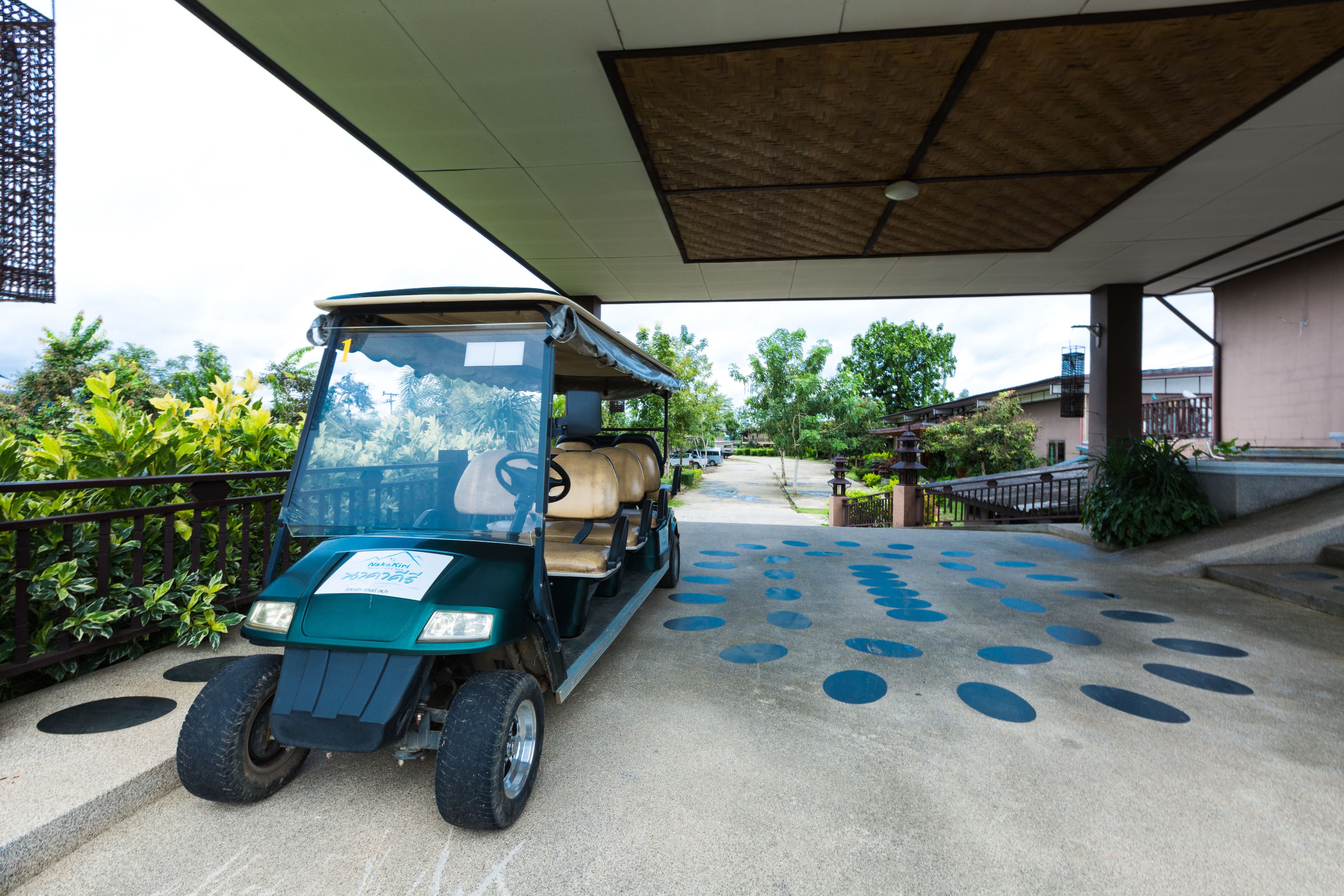 A golf cart parked on a concrete path with a patterned surface, surrounded by greenery and a building in the background.