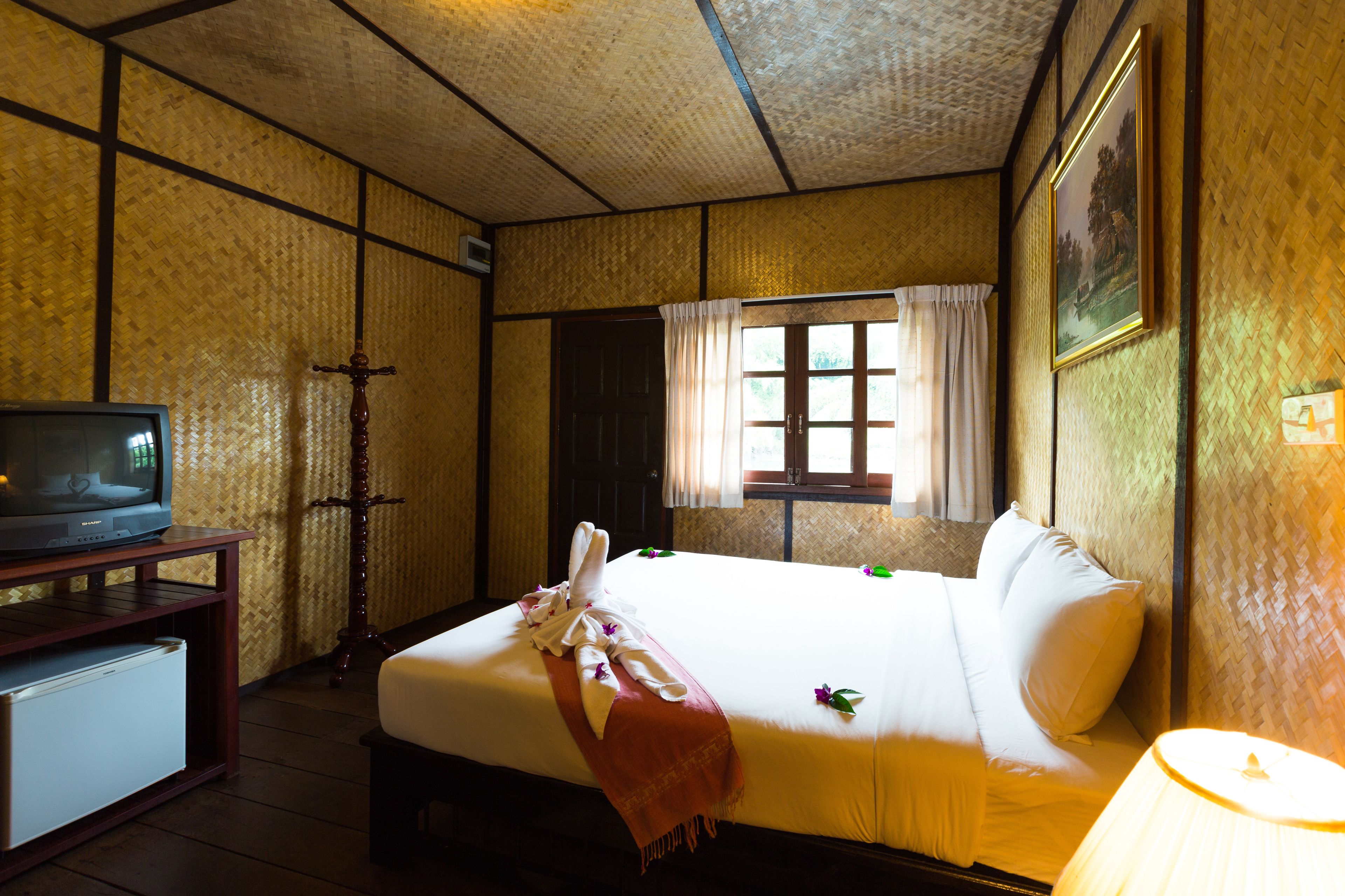 Een hotelkamer met een bed, een televisie op een houten tafeltje, een raam met gordijnen en een schilderij aan de muur.