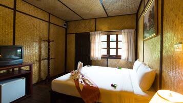 Een hotelkamer met een bed, een televisie op een houten tafeltje, een raam met gordijnen en een schilderij aan de muur.