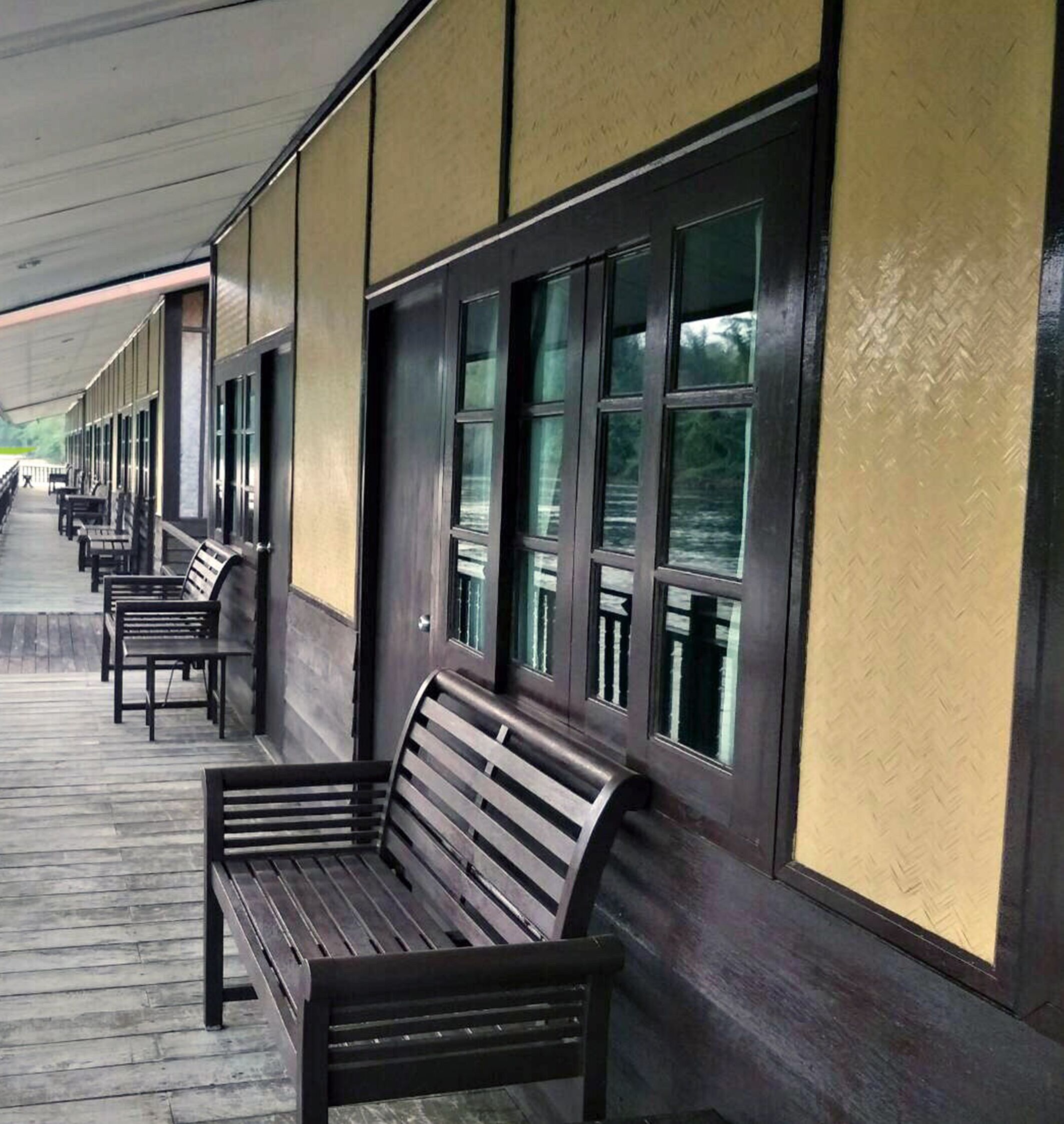 A covered outdoor seating area with benches and large windows along a wall.