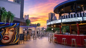 Un bar en la azotea con vista al horizonte de la ciudad, un mural y un letrero que anuncia Cosmopolitan Old Fashioned Mojito.