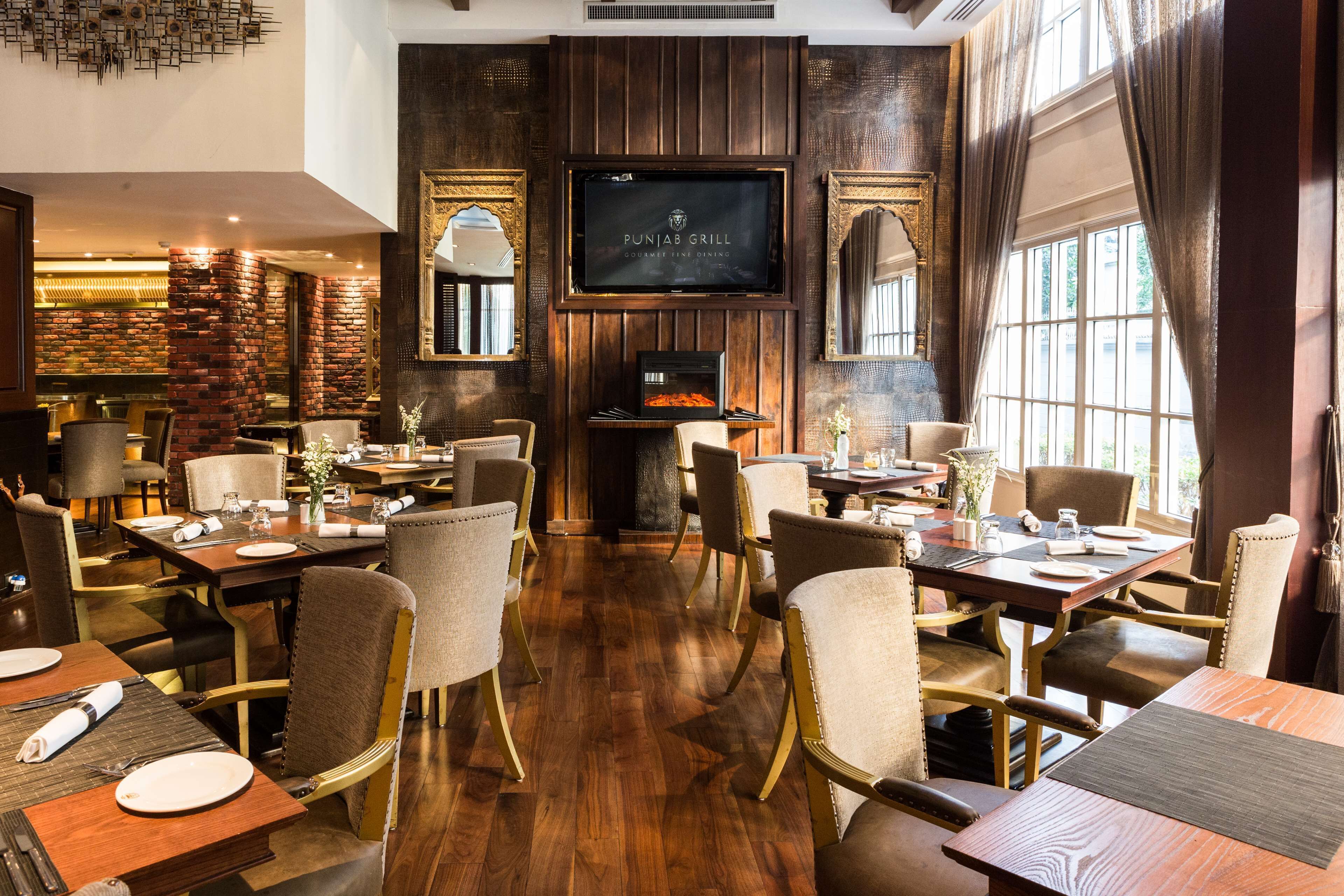 A restaurant with wooden flooring, multiple dining tables, and chairs, a television screen, and a brick wall.