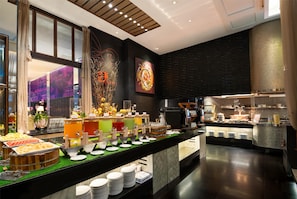 Ein Buffetbereich mit verschiedenen Speisen, eine Küche im Hintergrund und ein modernes Interieur.