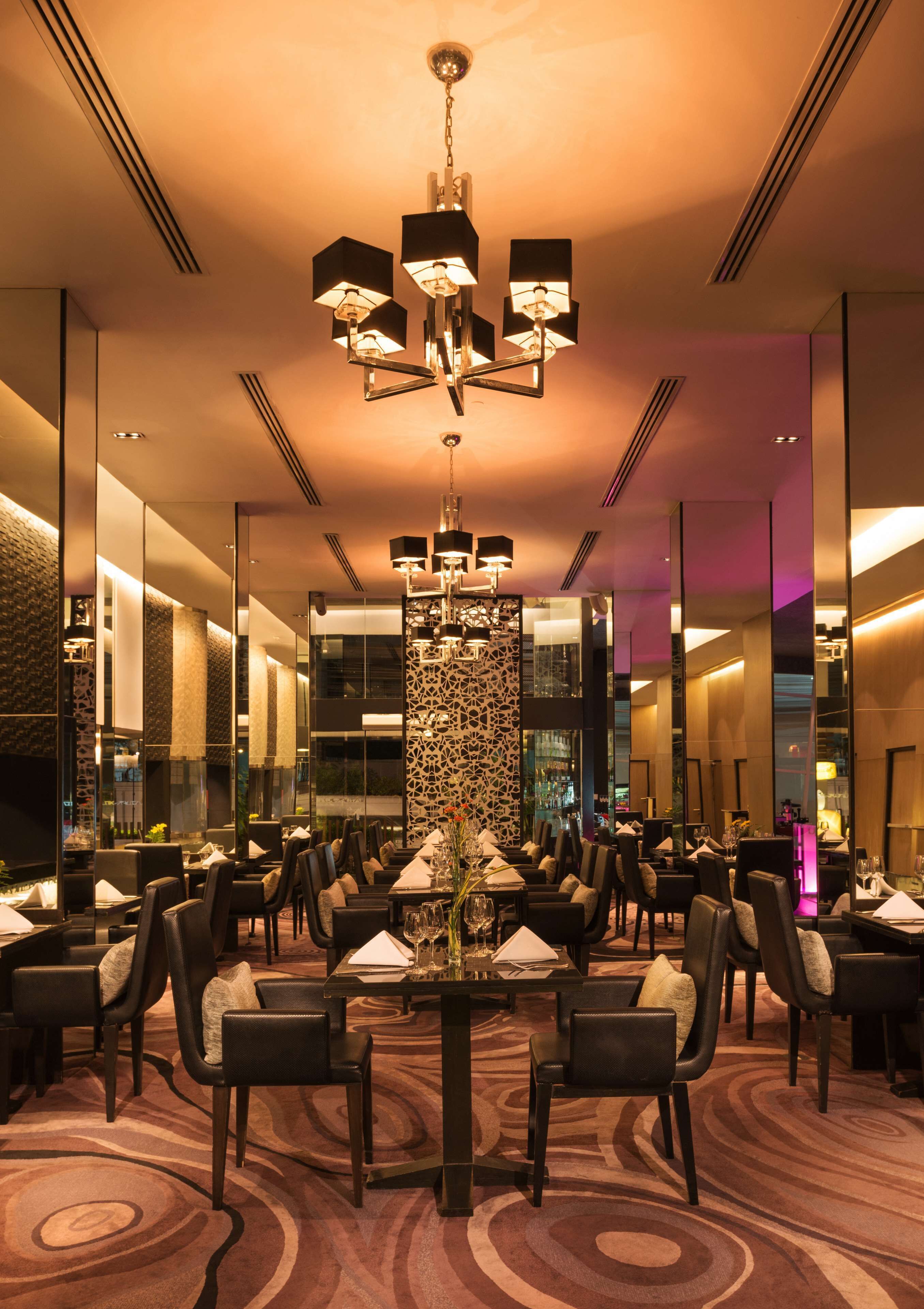 Un comedor de hotel con candelabro, paredes espejadas y alfombra estampada.