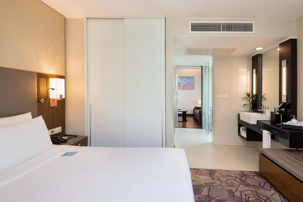 A hotel room with a bed, bedside table, lamp, and a view into the bathroom.