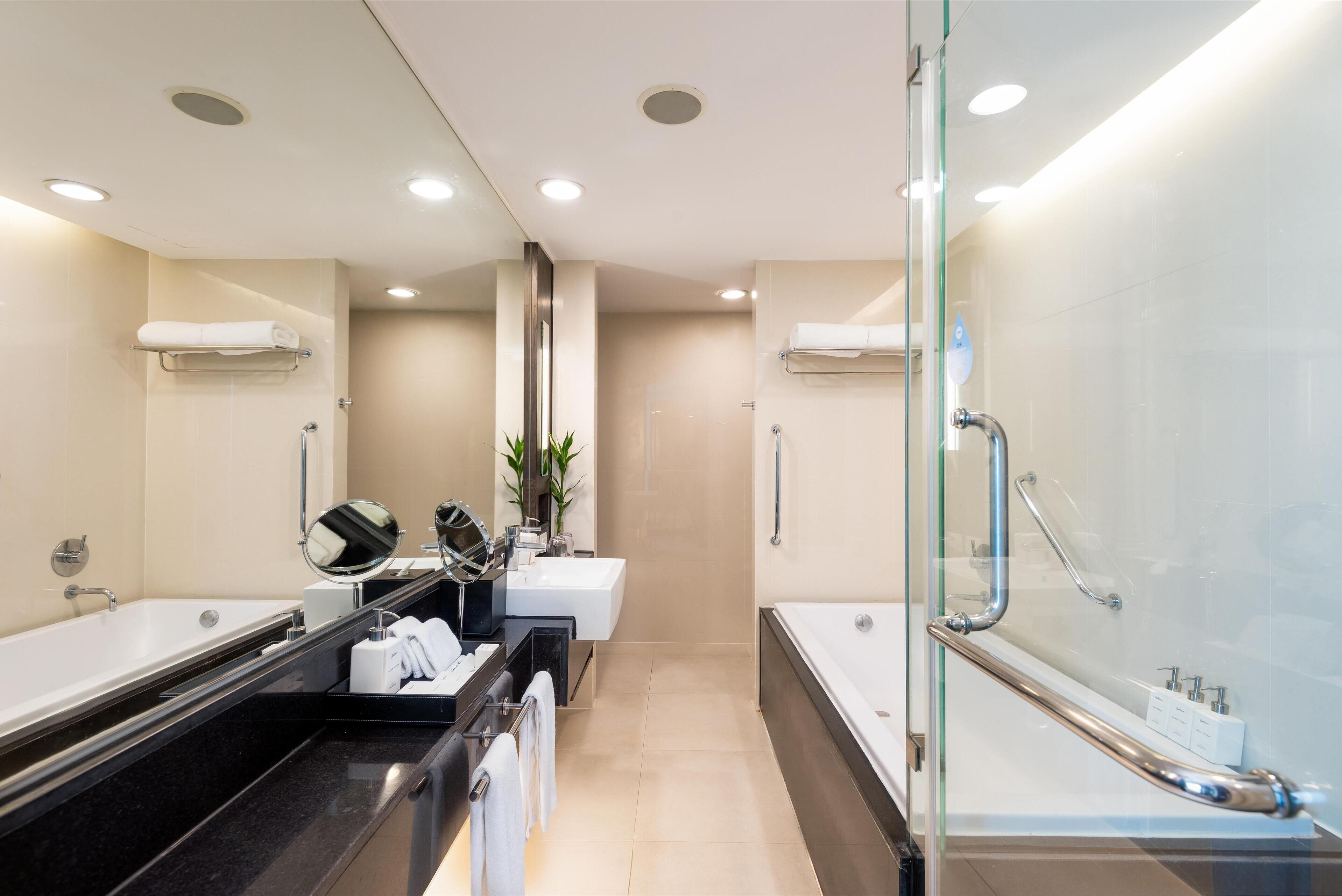 A modern bathroom with two sinks, a bathtub, and a glass shower enclosure.