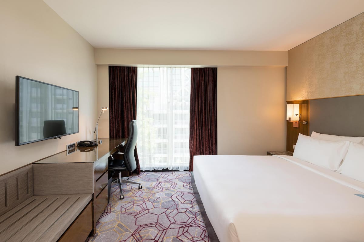 Ein Hotelzimmer mit einem Bett, einem Schreibtisch mit Stuhl, einem Fernseher und einem großen Fenster mit Vorhängen.
