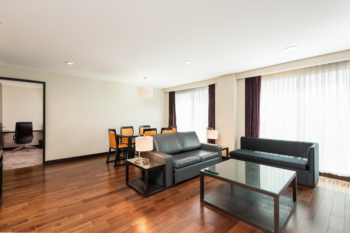 Ein modernes Hotelzimmer mit einer Couch, einem Glastisch, einem Schreibtisch mit Stuhl und einem Essbereich mit Stühlen und Tisch.