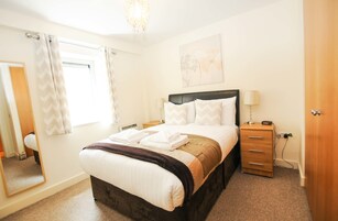A neatly arranged bedroom with a bed, bedside table, and a mirror.