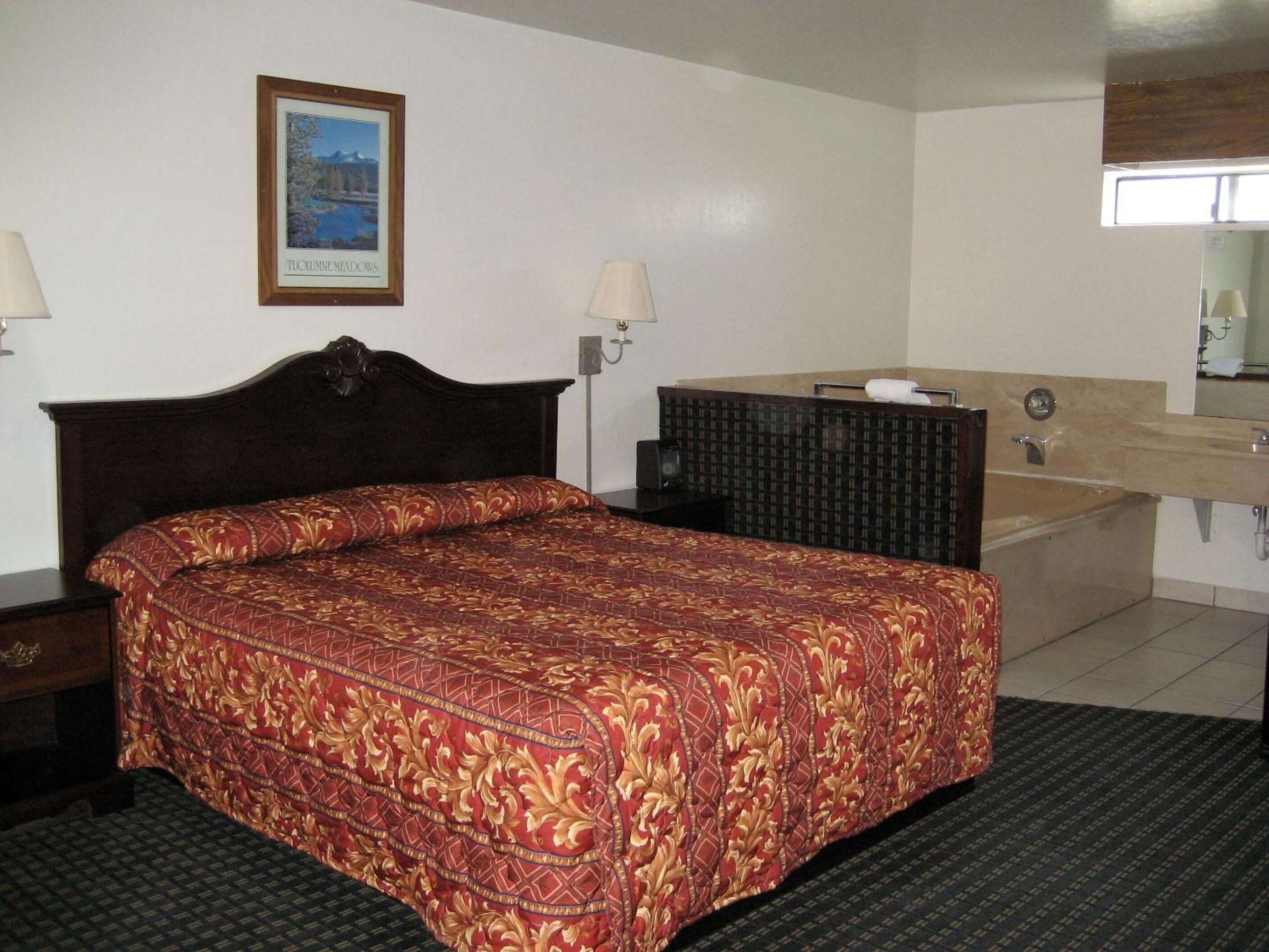 A hotel room with a large bed, a bedside table, a dresser, a mirror, and a bathroom with a sink and toilet.