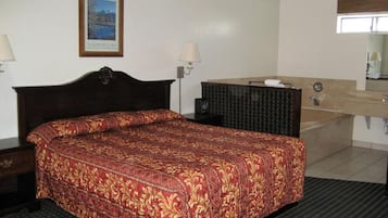 A hotel room with a large bed, a bedside table, a dresser, a mirror, and a bathroom with a sink and toilet.