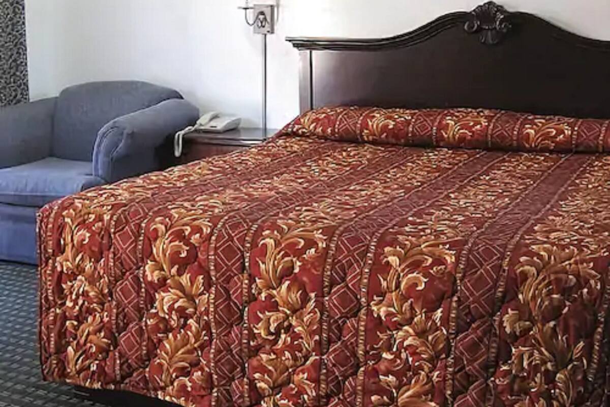 Een hotelkamer met een bed, een stoel, een nachtkastje, een lamp en een lijst met een foto aan de muur.