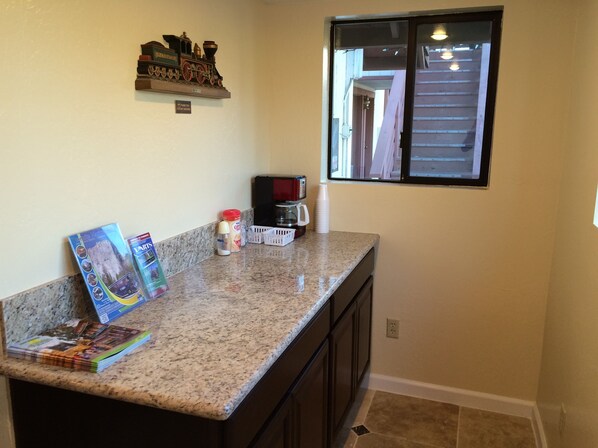 A kitchen with granite countertops, a coffee maker, and a window with a view of a building. - Jamestown Railtown Motel (Jamestown)