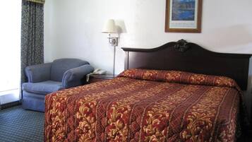 A hotel room with a bed, a chair, a lamp, and a framed picture on the wall.