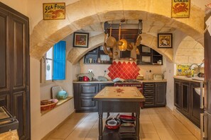 A kitchen with stone arches, a stove, hanging pots, and a tiled backsplash.