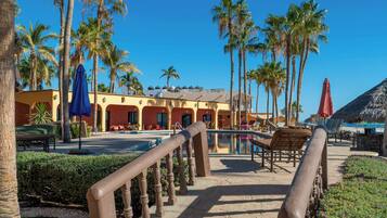 A resort with a pool, palm trees, and a thatched-roof building.
