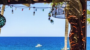 A wooden deck with tables and chairs overlooking a clear blue sea, with boats visible in the distance. - Playa del Sol (Los Barriles)
