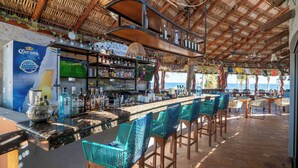 A bar with a thatched roof, a variety of bottles, and a view of the sea. - Playa del Sol (Los Barriles)