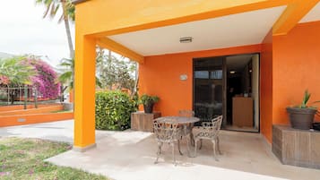 Un patio al aire libre con una mesa y sillas, rodeado de plantas en macetas y vista hacia la entrada de un edificio.