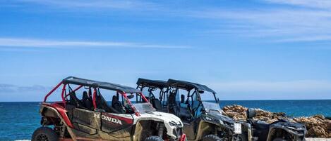 Three off-road vehicles parked on a rocky beach with the ocean in the background.