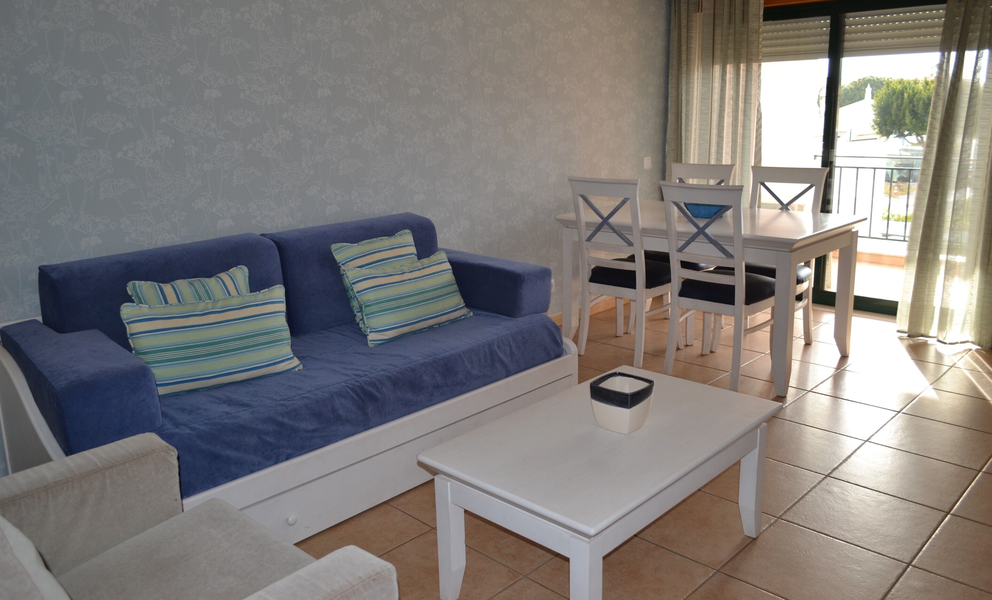 A living area with a blue sofa, striped pillows, a white coffee table, and a dining table with chairs.