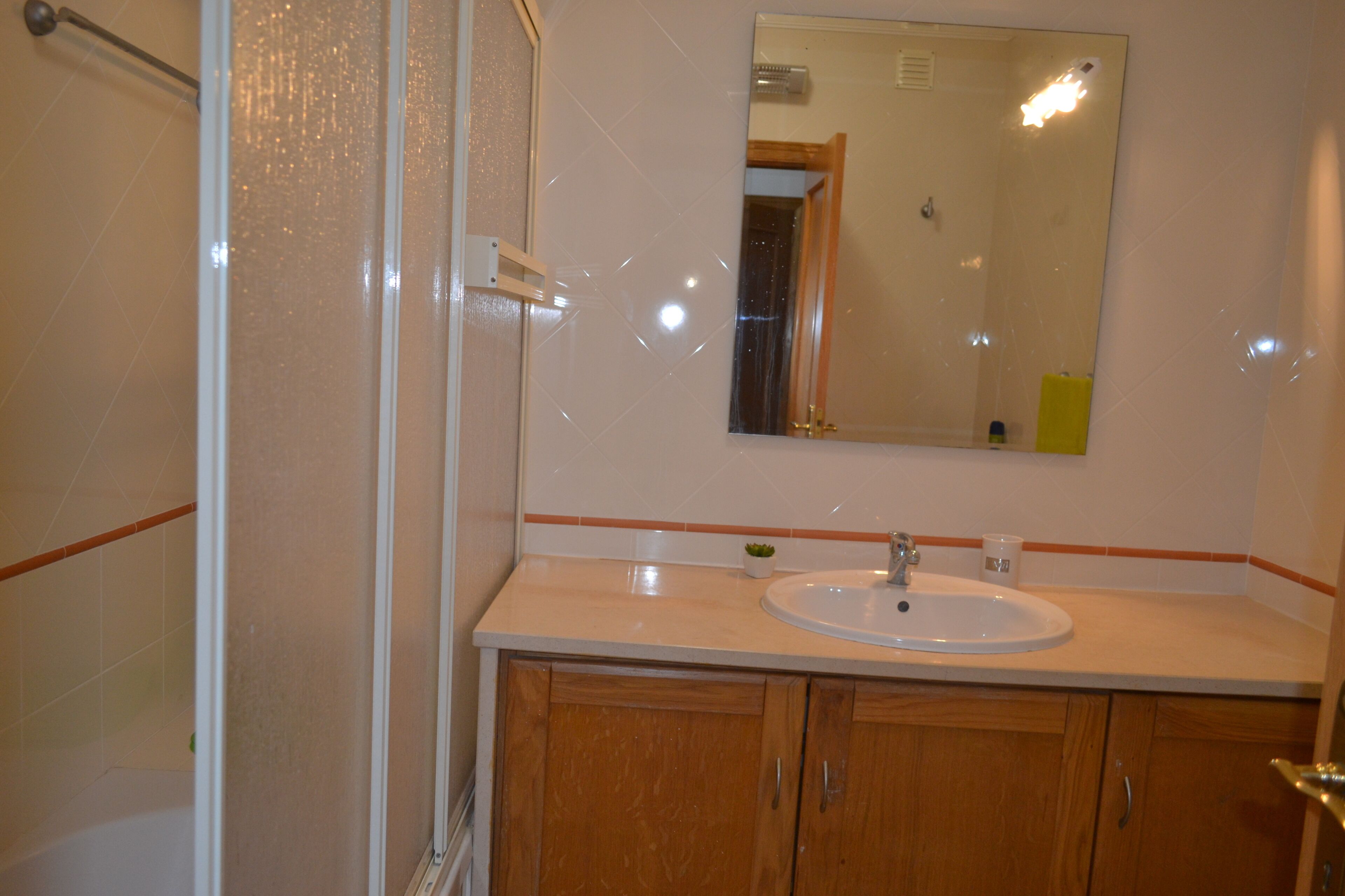 A bathroom with a shower, a sink, and wooden cabinets.