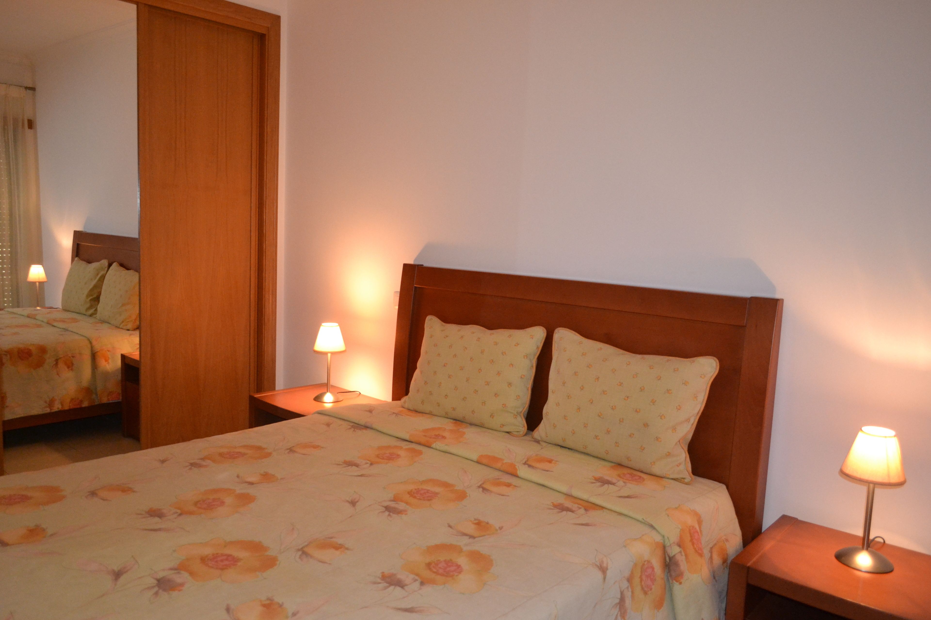A neatly made bed with floral bedding, two bedside lamps, and a wooden headboard.