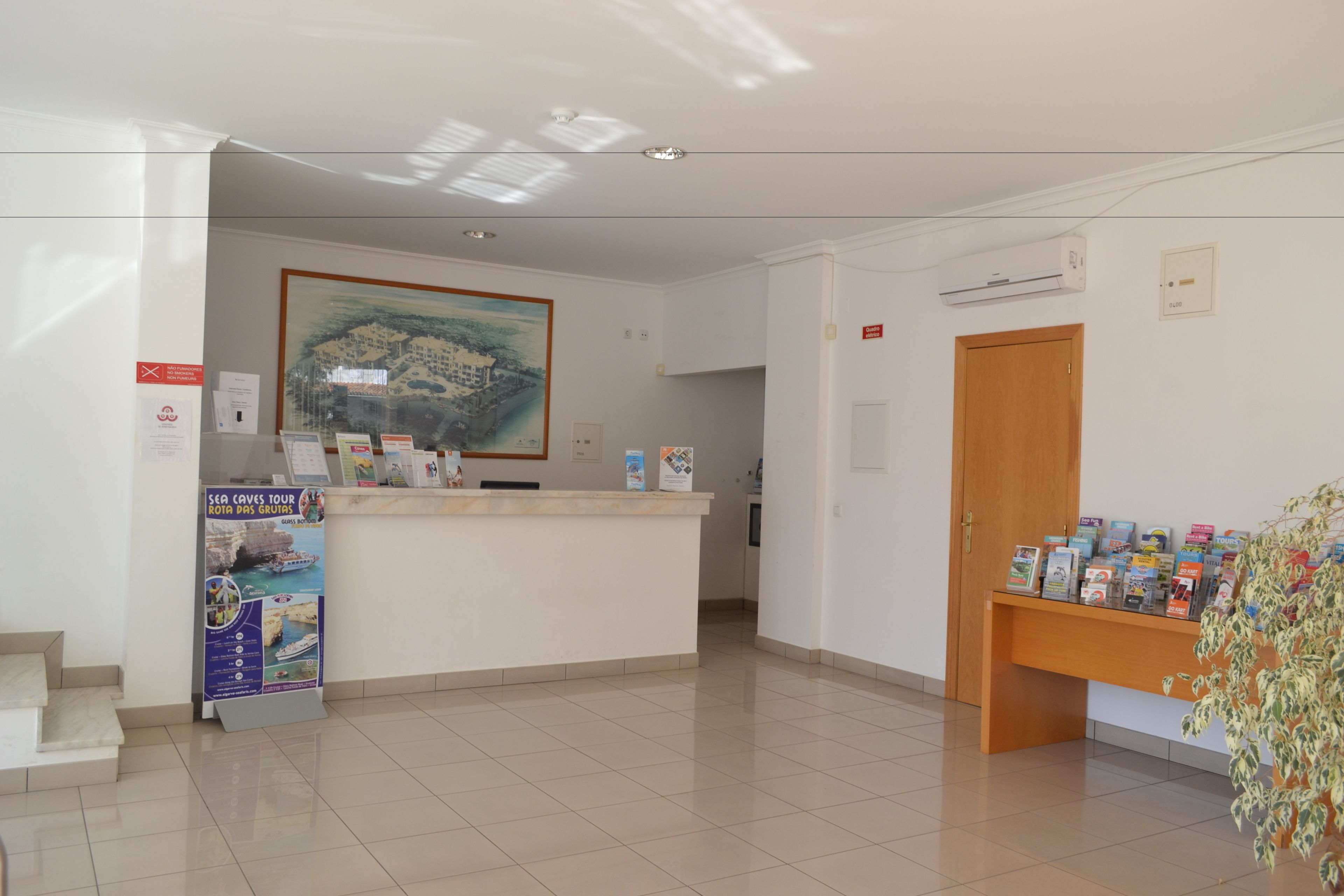 Un'area reception con un banco, un quadro incorniciato, un poster, una porta in legno e una pianta.