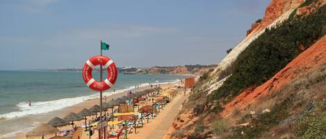 A beach with a lifebuoy, umbrellas, and a wooden walkway.