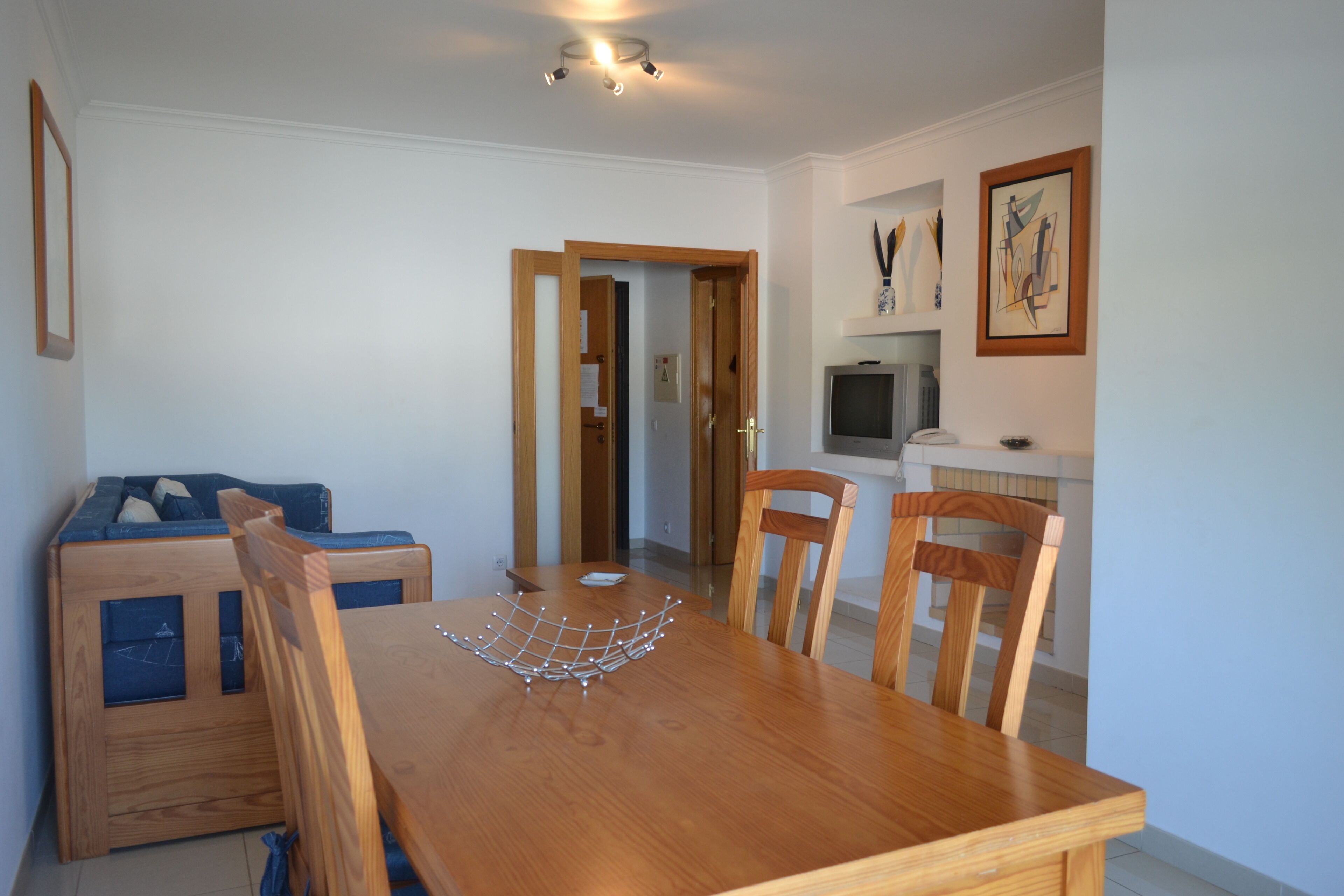 A dining area with a wooden table and chairs, a small sofa, and a television on a stand.