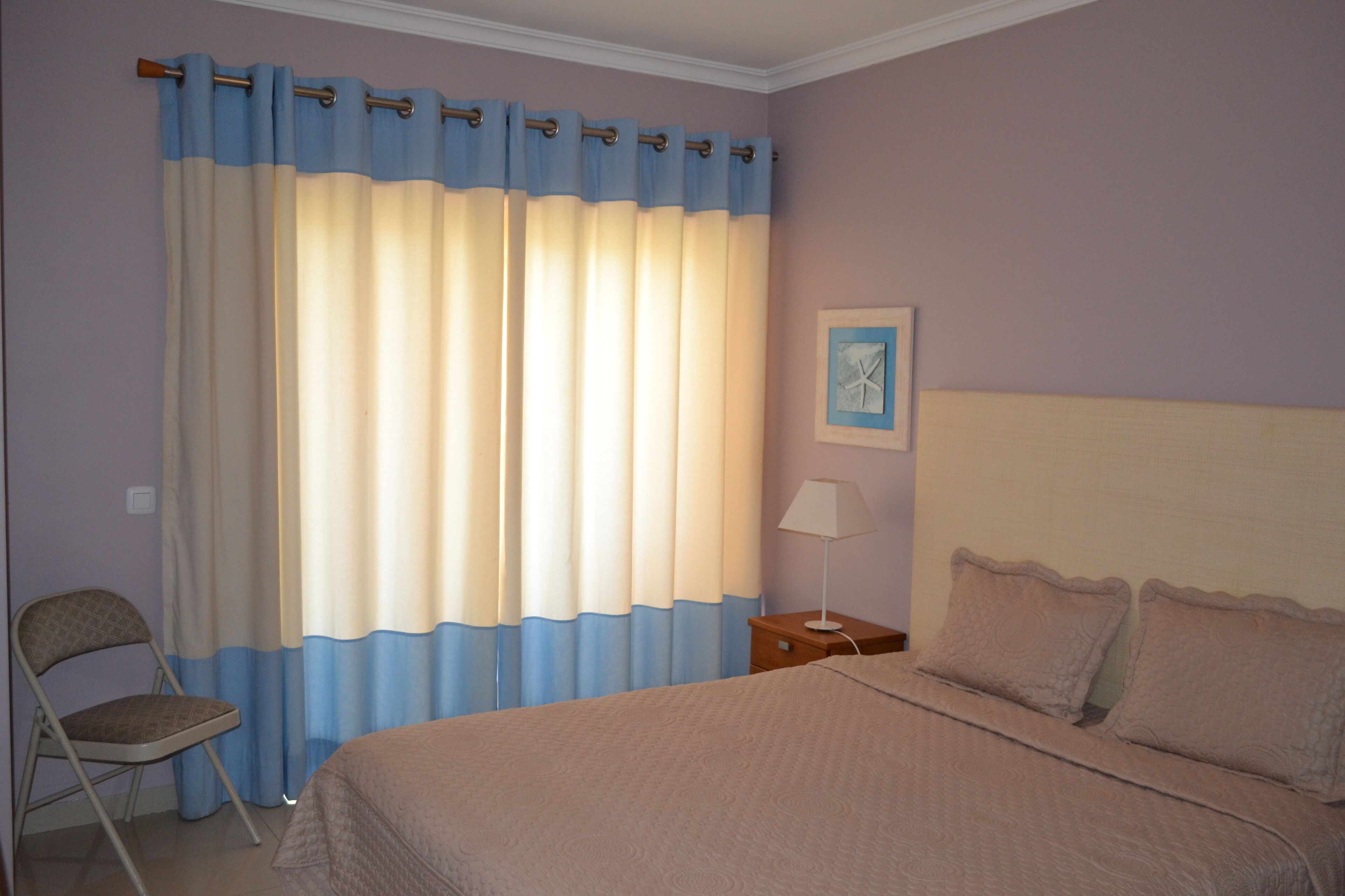 A bedroom with a bed, a chair, a nightstand, a lamp, and a wall art piece.