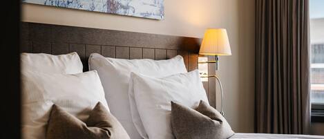 Una camera d'albergo con un letto, cuscini, un comodino, una lampada e un quadro appeso al muro.