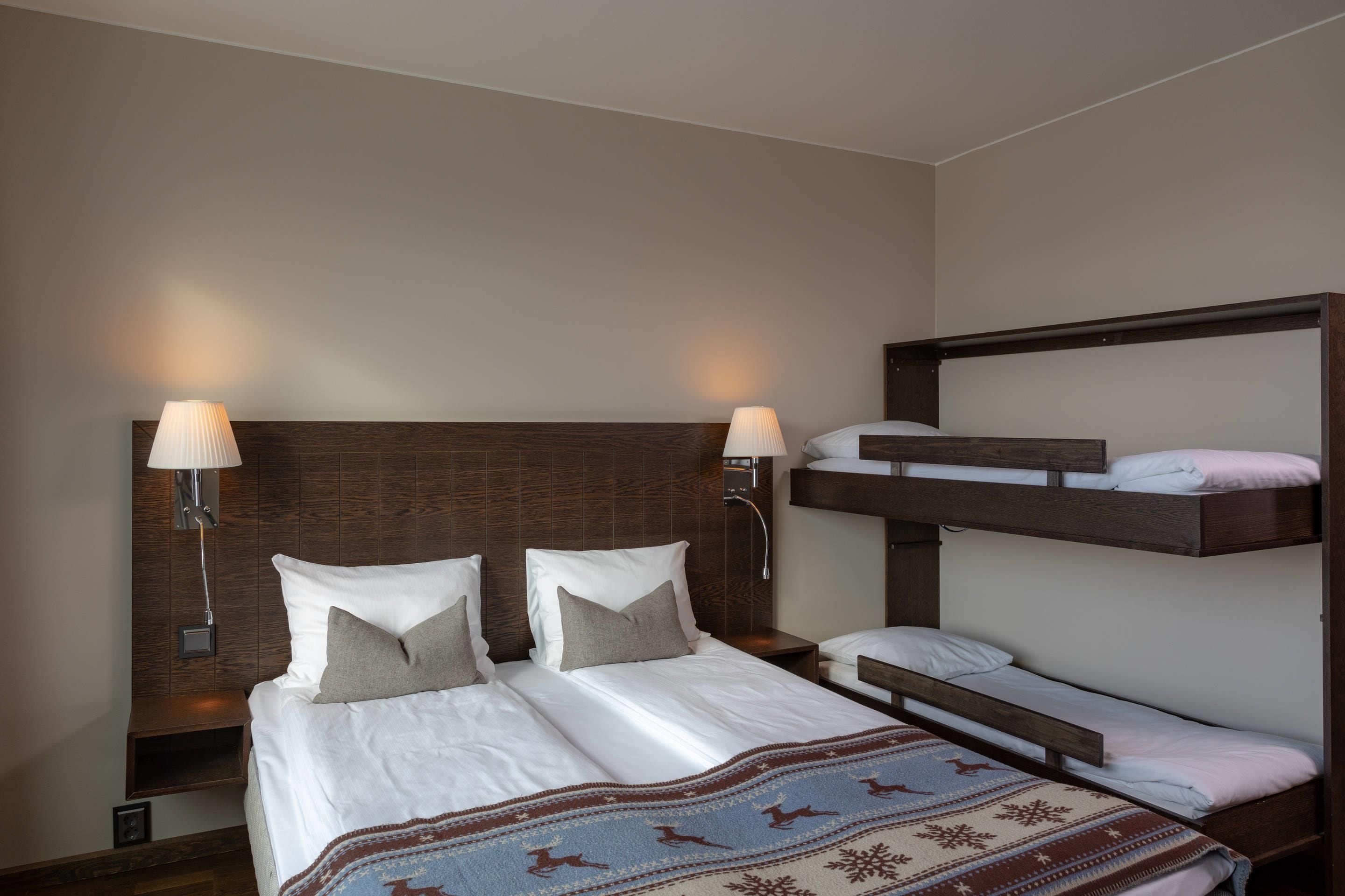 A bunk bed room with two bedside tables, each with a lamp, and a decorative blanket on the lower bed.
