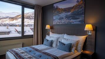 A hotel room with a large window, a bed with pillows, a bedside table, and a wall-mounted lamp.