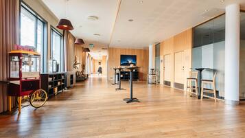 Un amplio vestíbulo de hotel con suelo de madera, una máquina de café y una zona de estar con mesas y sillas.